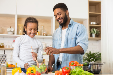 Cheerful dad seasoning salad, cooking with daughter