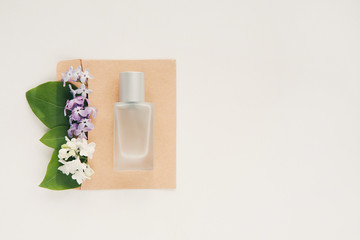 Bouquet of spring flowers in craft envelope, perfume spray bottle on white background. Copy space for your text. Top view. Perfumery and floral scent concept