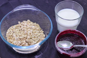 The ingredients for a healthy breakfast are oatmeal, milk, and berry jam. Morning light meal.