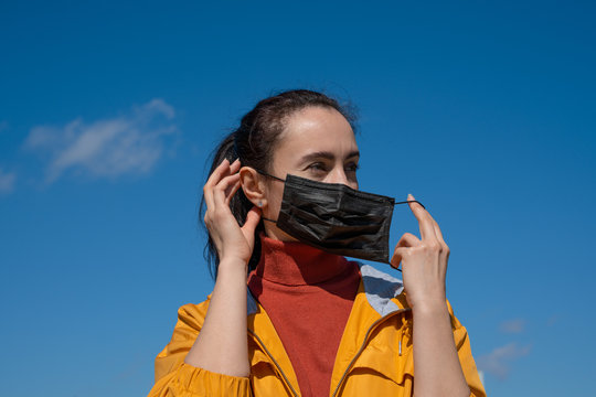 young woman wearing facial mask standing outdoors on sunny spring day
