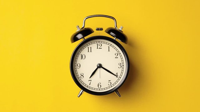 Time on vintage black alarm clock running from 7.00 to 8.00 isolated on yellow background color. One hour time lapse of black alarm clock running from 7.00 to 8.00.