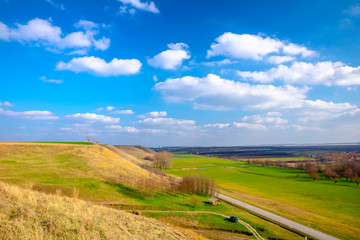 Fototapeta na wymiar Green hilly landscape and blue cloudy sky