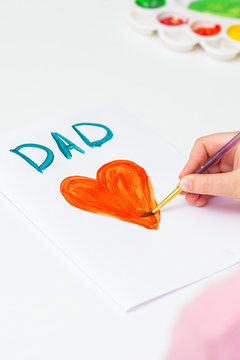 Hand of child drawing red heart with word Dad greeting card on white paper. Family and Father's Day concept.