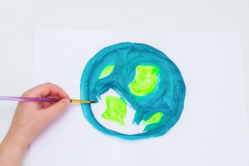 Child's hand drawing a planet Earth with a map of the world by watercolors on white paper. Peace...