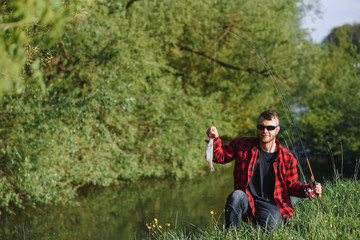 Naklejka na ściany i meble fisherman by the river with a catch of fish. Man fisherman holds in hand fish.