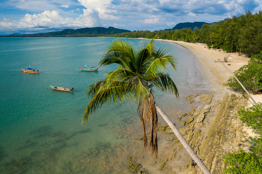 Aerial view of a beautiful, empty tropical beach surrounded by palm trees with small wooden fishing boats