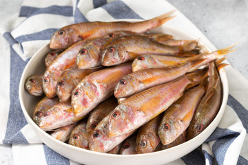 Black sea barabulka fish in a white ceramic bowl on a light gray kitchen table. A lot of fish red mullet. Black sea barabulka