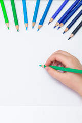 Top view of the child's hand painting on a white sheet of paper with colored pencils. Empty space for your text. Mockup.