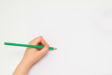 Top view of kid's left hand holding color pencil and drawing on white blank paper. Copy space for text. Mockup.