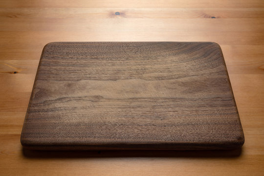 Handmade black walnut wooden chopping board with traces of knife carving on the table. Cutting board on wooden background.