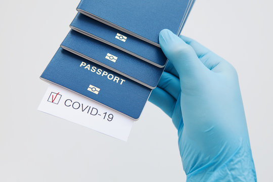 Immunity passport, risk-free certificate concept. Hands in medical gloves hold passports with note COVID-19 coronavirus with red check mark. Coronavirus outbreak situation, traveling after pandemic  - Powered by Adobe