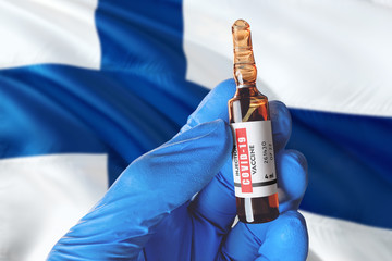 Finland flag with Coronavirus Covid-19 concept. Doctor with blue protection medical gloves holds a...