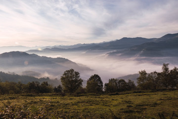 View from above of a valley covered by mist and some mountains with a partially cloud sky
