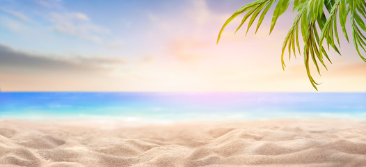A summer vacation, holiday background of a tropical beach and blue sea at sunset with green palm tree leaves.
