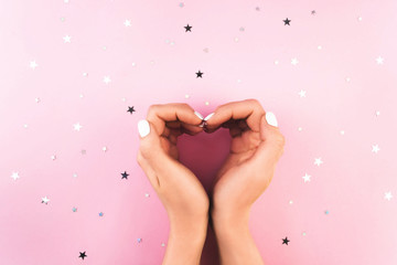 Love heart shape gesture. Two young woman's hands with perfect white manicure on pink background...