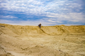 Fototapeta na wymiar Motorcyclist on a sand quarry against the sky with clouds in the summer