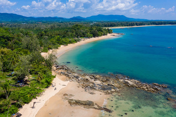 Aerial view of a beautiful, empty tropical beach surrounded by lush green foliage