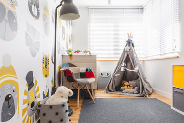 Grey tent with toys,colorful armchair, grey lamp and rug in small kid's playroom