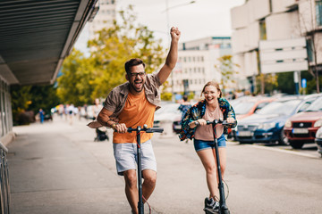 Young couple on vacation having fun driving electric scooter through the city.
