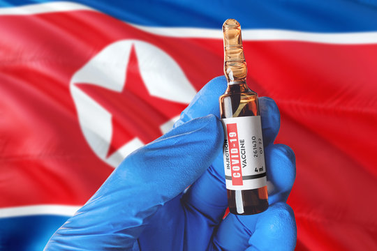 North Korea Flag With Coronavirus Covid-19 Concept. Doctor With Blue Protection Medical Gloves Holds A Vaccine Bottle. Coronavirus Covid 19 Vaccine Research.