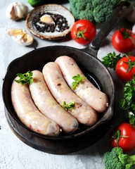 Raw homemade sausages (chicken, turkey) in a pan on a gray background with vegetables. Still life