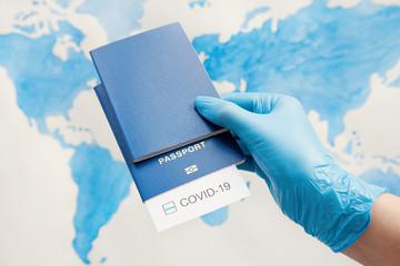 Immunity passport, risk-free certificate concept. Hand in medical gloves holds passports with note COVID-19 and green check mark on world map. Coronavirus outbreak situation, traveling after pandemic
