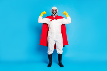 Full body photo strong confident medical worker show muscles stop biological covid19 danger epidemic wear red mantle costume white suit yellow gloves goggles isolated blue color background
