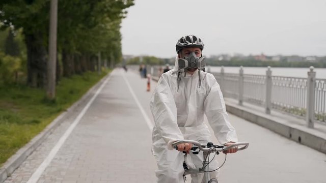 Front view of a young man in a protective suit, mask and helmet rides a bicycle