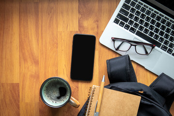 Work space with a laptop, smart phone and a cup of coffee. There are a glasses on touch pad. A book and a pen is on a backpack . There are space for text on wood floor. Work from home concept.