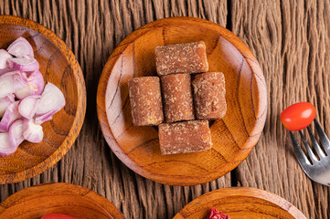 Palm sugar and red onions on a wooden plate with a tomato skewer on the wooden floor.