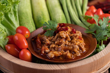 Sweet pork in a wooden bowl with cucumber, long beans, tomatoes, and side dishes.