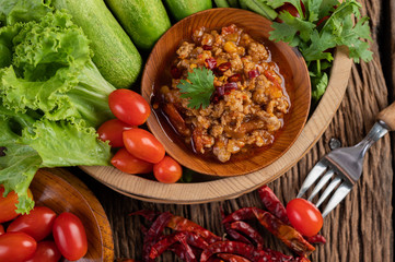Sweet pork in a wooden bowl with cucumber, long beans, tomatoes, and side dishes.