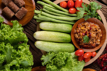Sweet pork in a wooden bowl with cucumber, long beans, tomatoes, and side dishes.