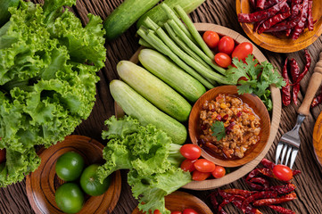 Sweet pork in a wooden bowl with cucumber, long beans, tomatoes, and side dishes.