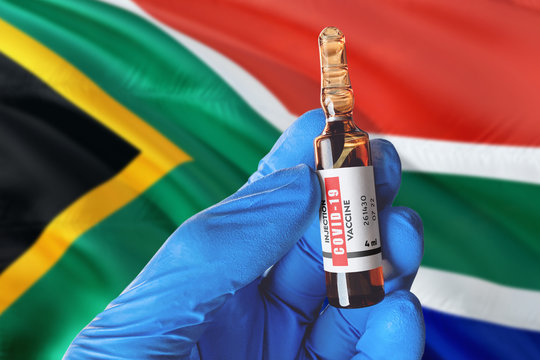 South Africa Flag With Coronavirus Covid-19 Concept. Doctor With Blue Protection Medical Gloves Holds A Vaccine Bottle. Coronavirus Covid 19 Vaccine Research.