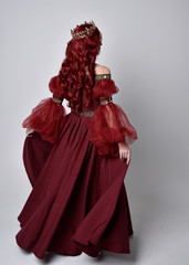 Portrait of a beautiful woman with red hair wearing  a  flowing Burgundy fantasy gown and golden...