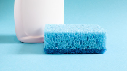 One blue sponge with a white bottle of detergent on a blue background. Convenience of sponges consists in good detergent retention that allows to use it economically