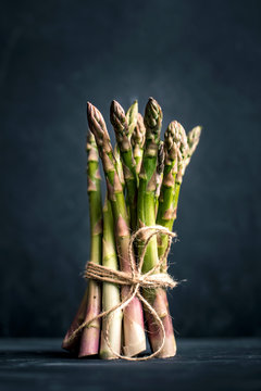 Fresh green uncooked asparagus on black background. Healthy raw green food. Bunch of  asparagus tied with twine.