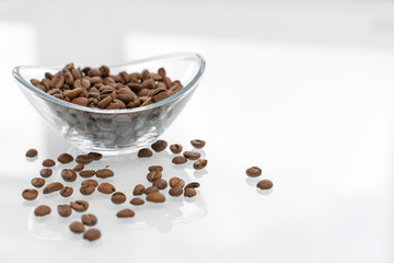 Coffee beans in a glass bowl on a glossy light table. some grains are scattered on the table. breakfast concept