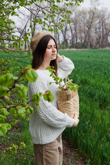 Beautiful stylish young woman in hat with wicker bag standing on field