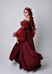Portrait of a beautiful woman with red hair wearing  a  flowing Burgundy fantasy gown and golden...