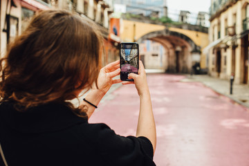 Young caucasian woman tourist taking photos with modern smartphone while standing on the Pink Street, famous night life place in Lisbon, Portugal. European travel destination concept