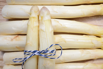 White fresh raw asparagus lies side by side on a wooden surface and is wrapped with a band