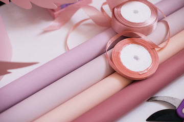 wrapping paper of bright pink, pale pink, salmon and purple with ribbons on a white table. preparation for packaging and decorating a bouquet of flowers for the holiday.