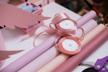 
wrapping paper of bright pink, pale pink, salmon and purple with ribbons on a white table. preparation for packaging and decorating a bouquet of flowers for the holiday.