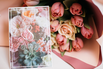 a bouquet of fresh pink and peach roses in paper packaging with a greeting card on a white table as a gift for the holiday
