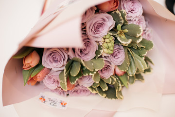 a bouquet of fresh purple roses in a beautiful pale pink packaging with a logo on a white table as a gift for the holiday