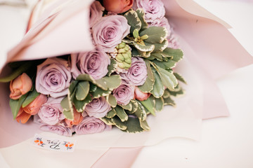 a bouquet of fresh purple roses in a beautiful pale pink packaging with a logo on a white table as a gift for the holiday
