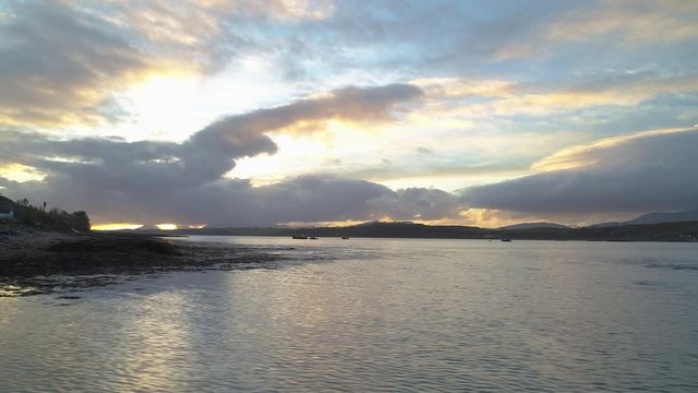 Fast and low aerial movement from coastline out to sea looking toward colourful sunset, Scotland UK