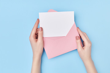 Pink envelope with blank white postcard in woman's hands on the blue background. Mail concept